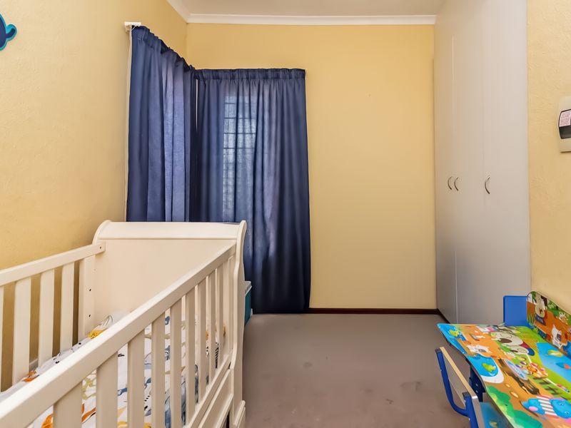 A bedroom featuring built-in cupboards, neutral wall finishes, and security bars on the window, providing a functional space for a nursery or child's room.