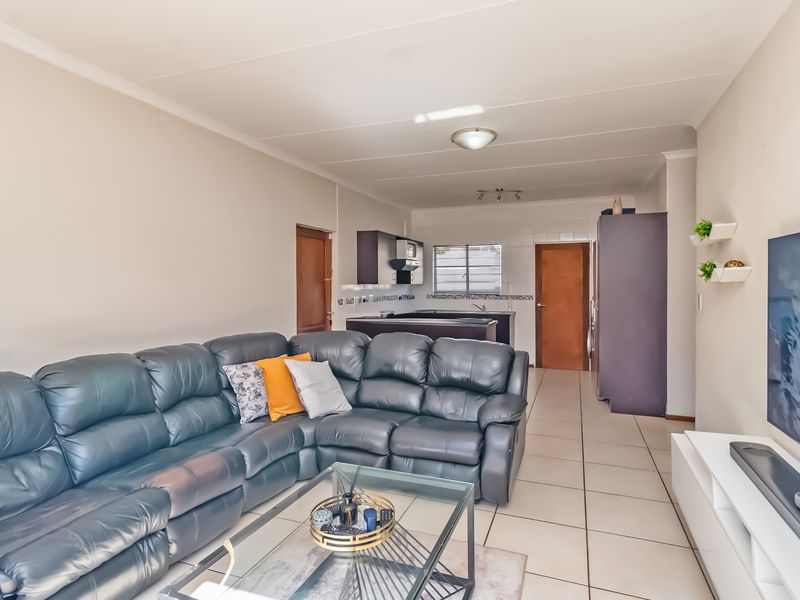 Open-plan living area featuring tiled flooring and a functional kitchen with built-in cabinetry and a tiled backsplash.