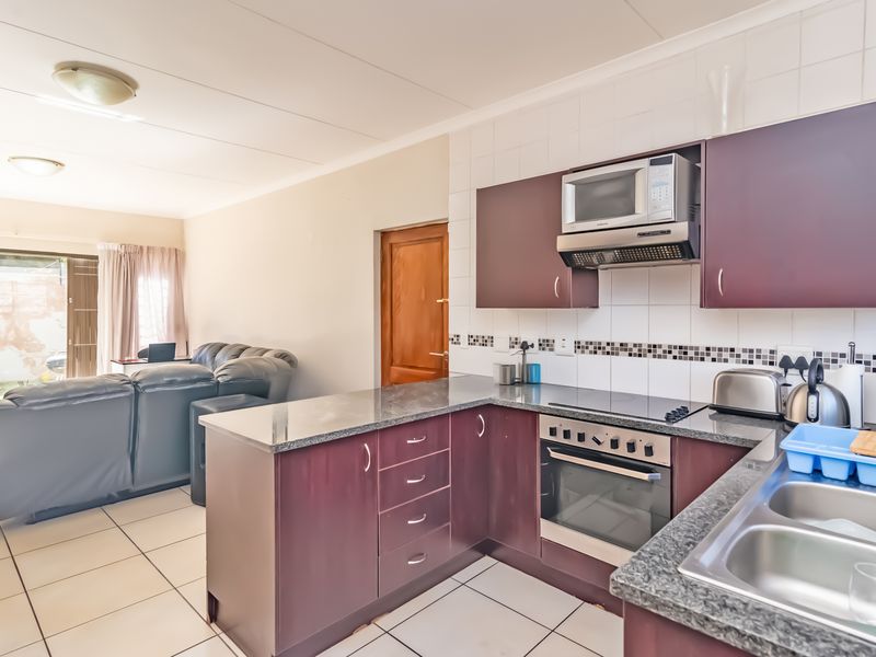 Open-plan kitchen and living area featuring dark wood cabinetry, granite countertops, built-in appliances, and tiled flooring with access to an outdoor patio.