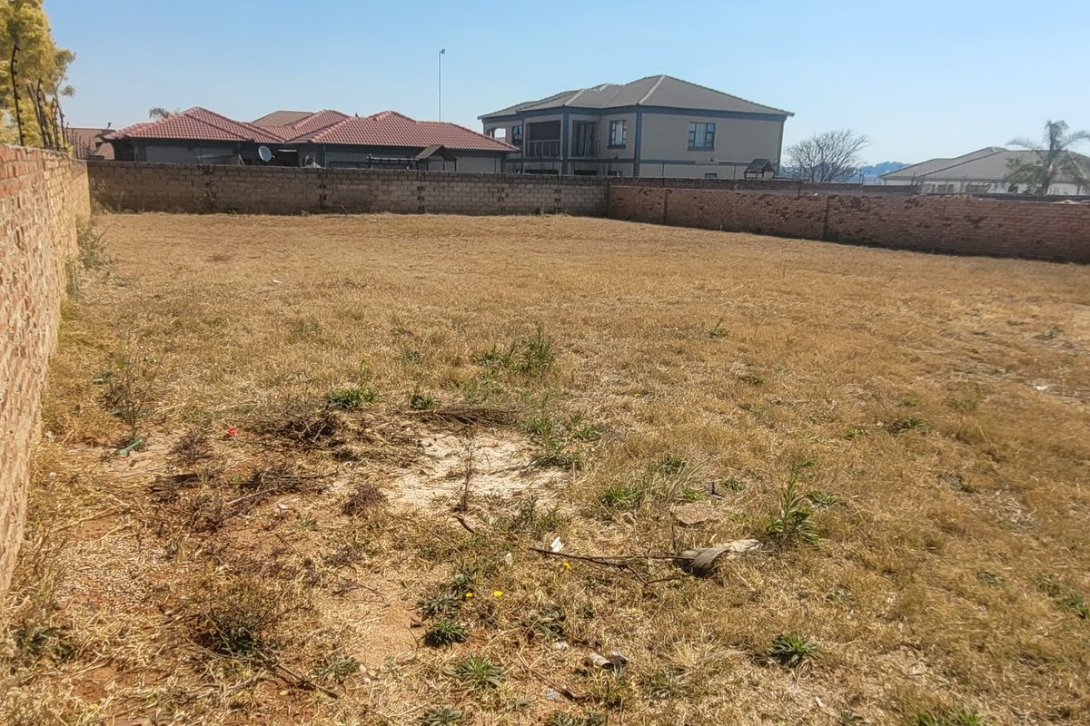 A vacant residential plot enclosed by perimeter brick walls, offering a clear space ready for development in a suburban neighborhood.
