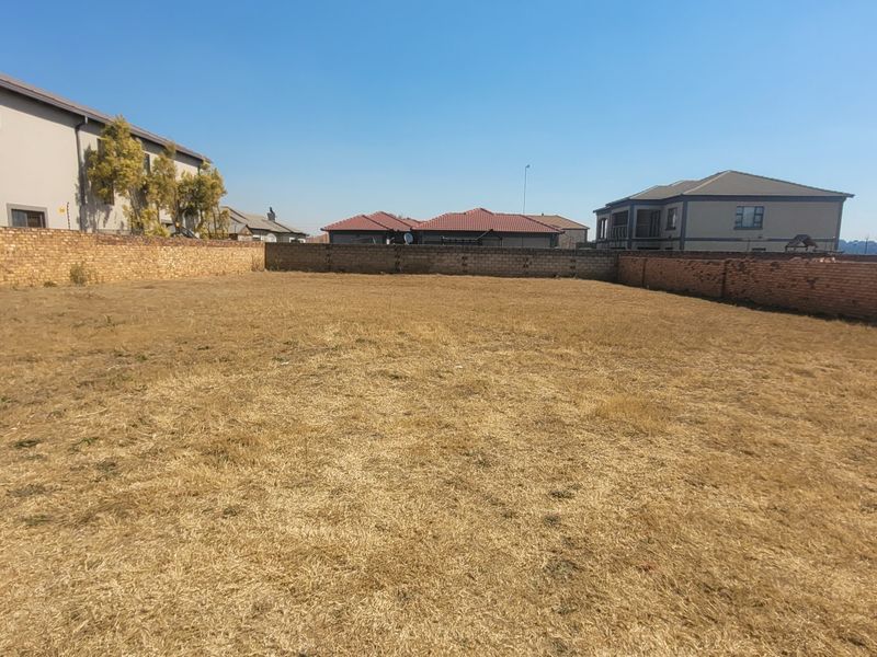A vacant residential plot featuring a level grass surface enclosed by perimeter brick boundary walls in a developed neighborhood.
