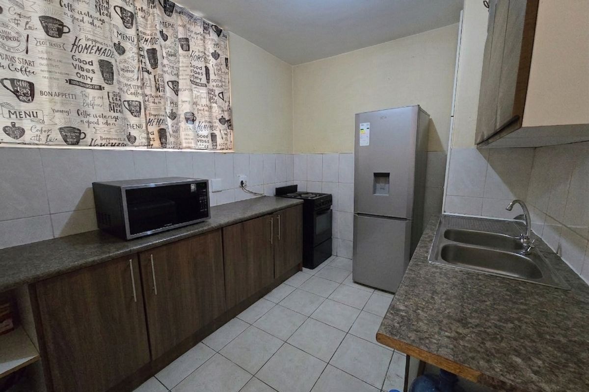 A functional kitchen featuring laminate countertops, double bowl sink, tiled splashback, and built-in cabinetry with a freestanding stove.
