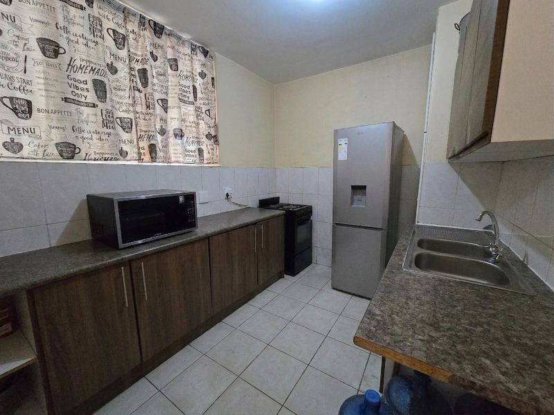 A functional kitchen featuring laminate countertops, double bowl sink, tiled splashback, and built-in cabinetry with a freestanding stove.
