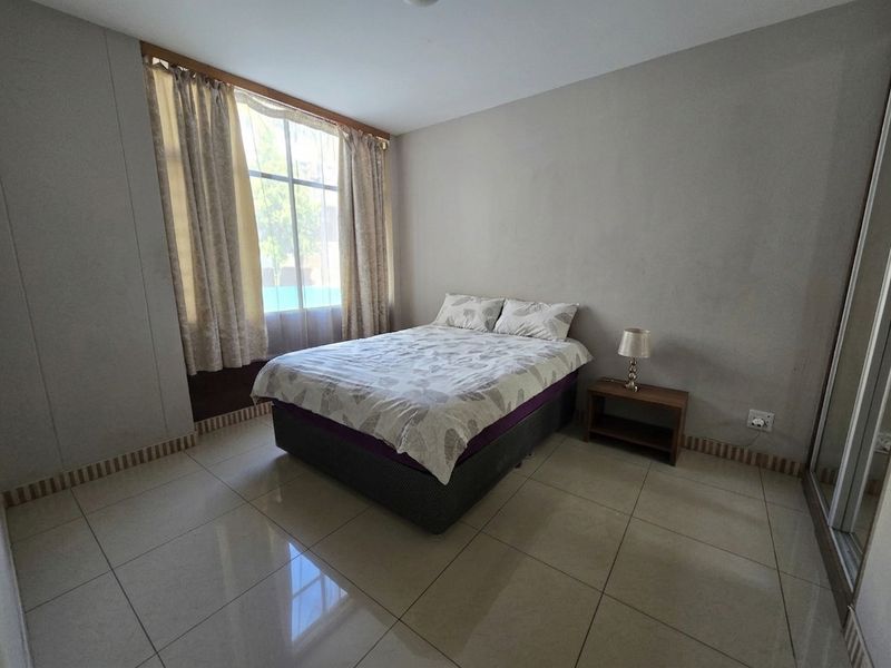 A bedroom featuring large windows, tiled flooring, and a built-in sliding door wardrobe.