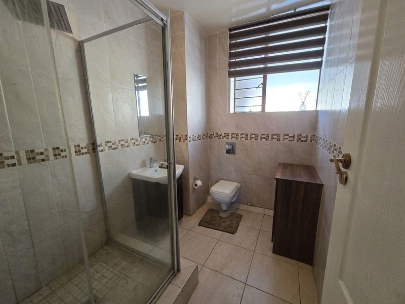 A well-maintained bathroom featuring a glass shower enclosure, wall-hung toilet, vanity basin, and neutral floor-to-ceiling tiling.