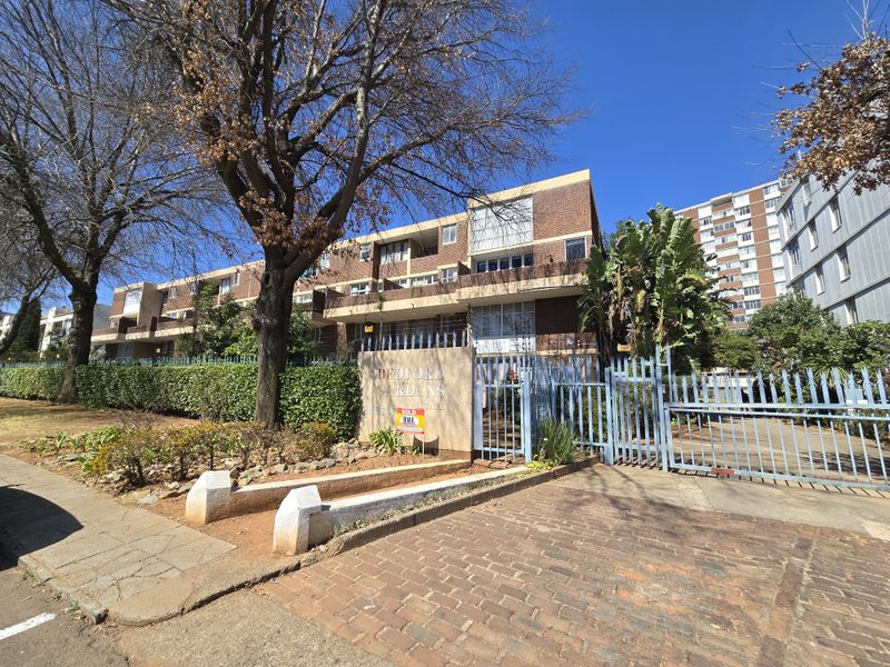 Front exterior view of a multi-story townhouse complex featuring brick facade, secure gated entrance, and established garden landscaping.
