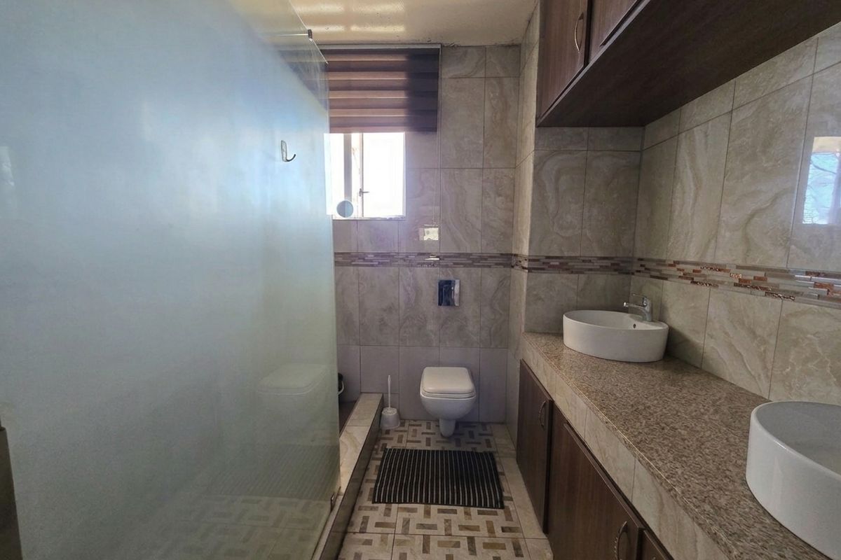 Modern bathroom featuring a double vanity with vessel sinks, granite countertops, wall-mounted toilet, and a spacious glass-enclosed shower with floor-to-ceiling tiling.