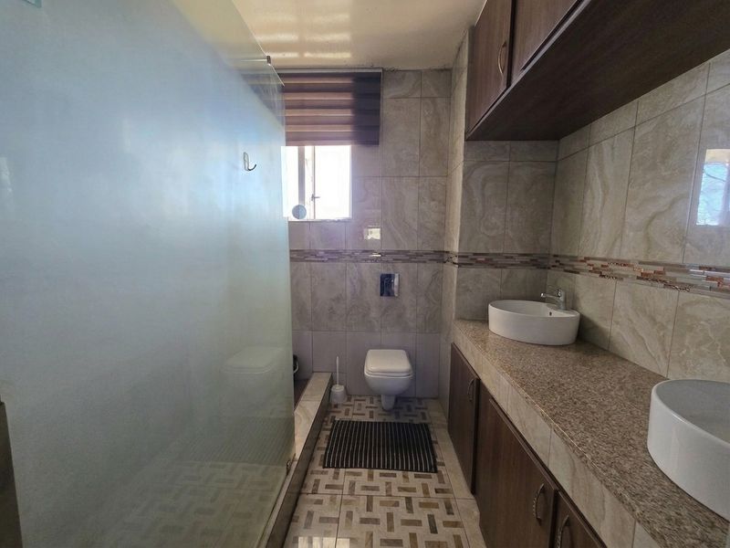 Modern bathroom featuring a double vanity with vessel sinks, granite countertops, wall-mounted toilet, and a spacious glass-enclosed shower with floor-to-ceiling tiling.