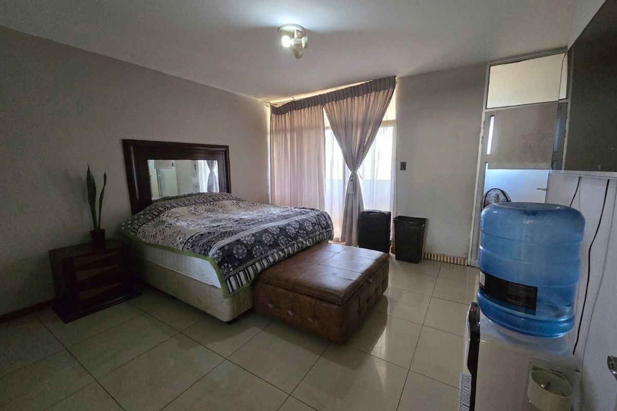A spacious bedroom featuring tiled flooring, neutral walls, and large windows with curtains, offering a functional and well-lit living space.