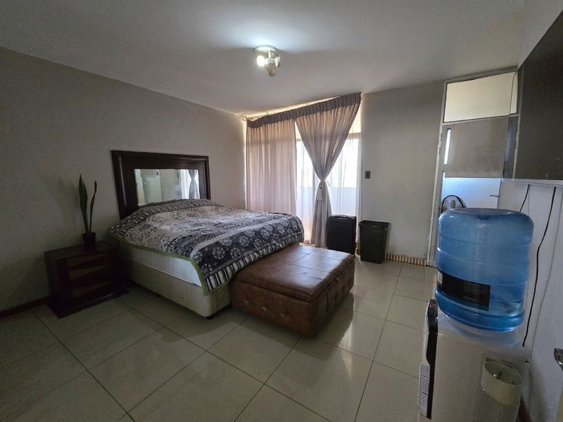 A spacious bedroom featuring tiled flooring, neutral walls, and large windows with curtains, offering a functional and well-lit living space.