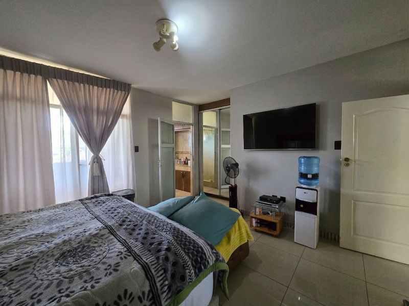 Spacious bedroom featuring tiled flooring, built-in cupboards, and direct access to an en-suite bathroom, offering a functional and comfortable living space.