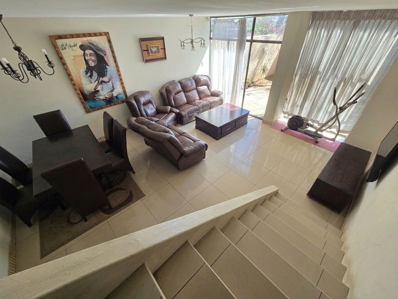 Spacious open-plan living and dining area featuring tiled flooring, a staircase, and large sliding glass doors providing access to the outdoor patio.
