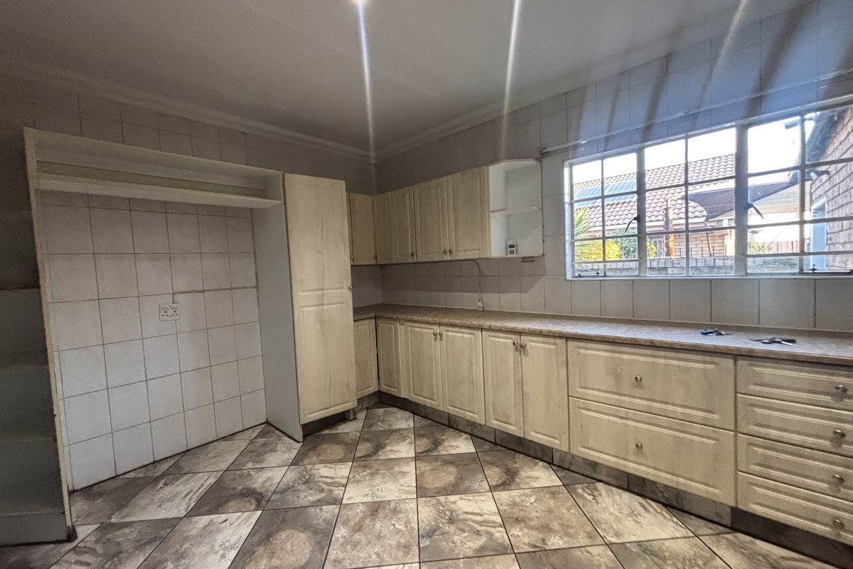 An empty kitchen featuring light-toned laminate cabinetry, tiled backsplash, and patterned floor tiles, offering a functional layout ready for modernization.