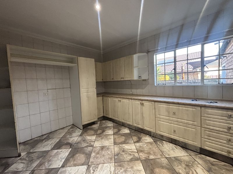 An empty kitchen featuring light-toned laminate cabinetry, tiled backsplash, and patterned floor tiles, offering a functional layout ready for modernization.