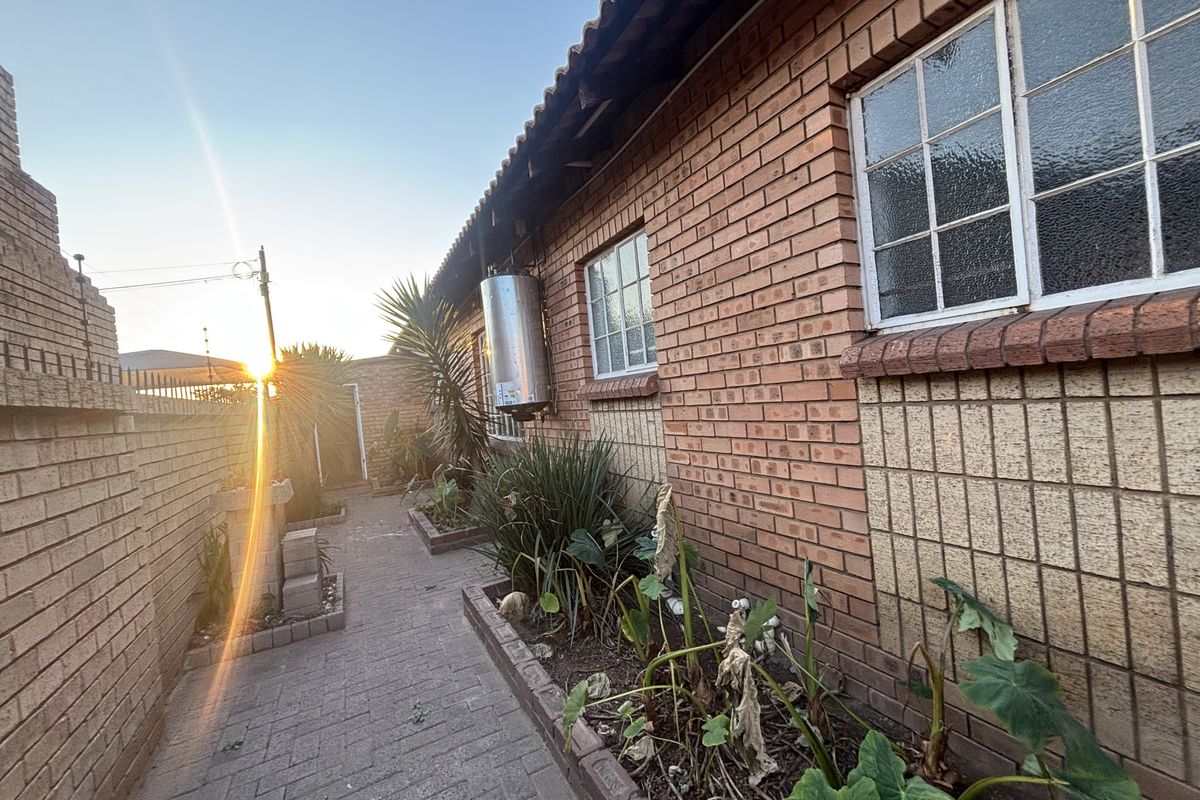 A side exterior view of the property featuring a paved walkway, brick facade, and an external electric geyser unit.