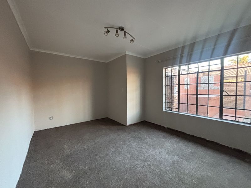 An empty bedroom featuring neutral walls, carpet flooring, and large windows with integrated security bars, offering a blank canvas for personalization.