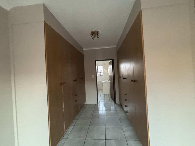 A hallway featuring extensive built-in wooden cabinetry and tiled flooring, leading towards an adjacent bathroom area.