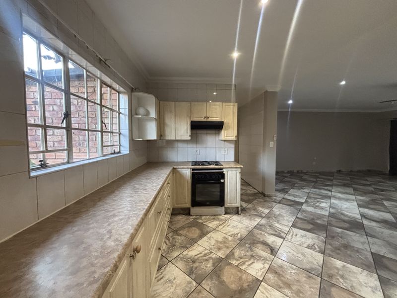 Open-plan kitchen featuring built-in cabinetry, laminate countertops, and integrated appliances, flowing into a spacious living area with tiled flooring throughout.