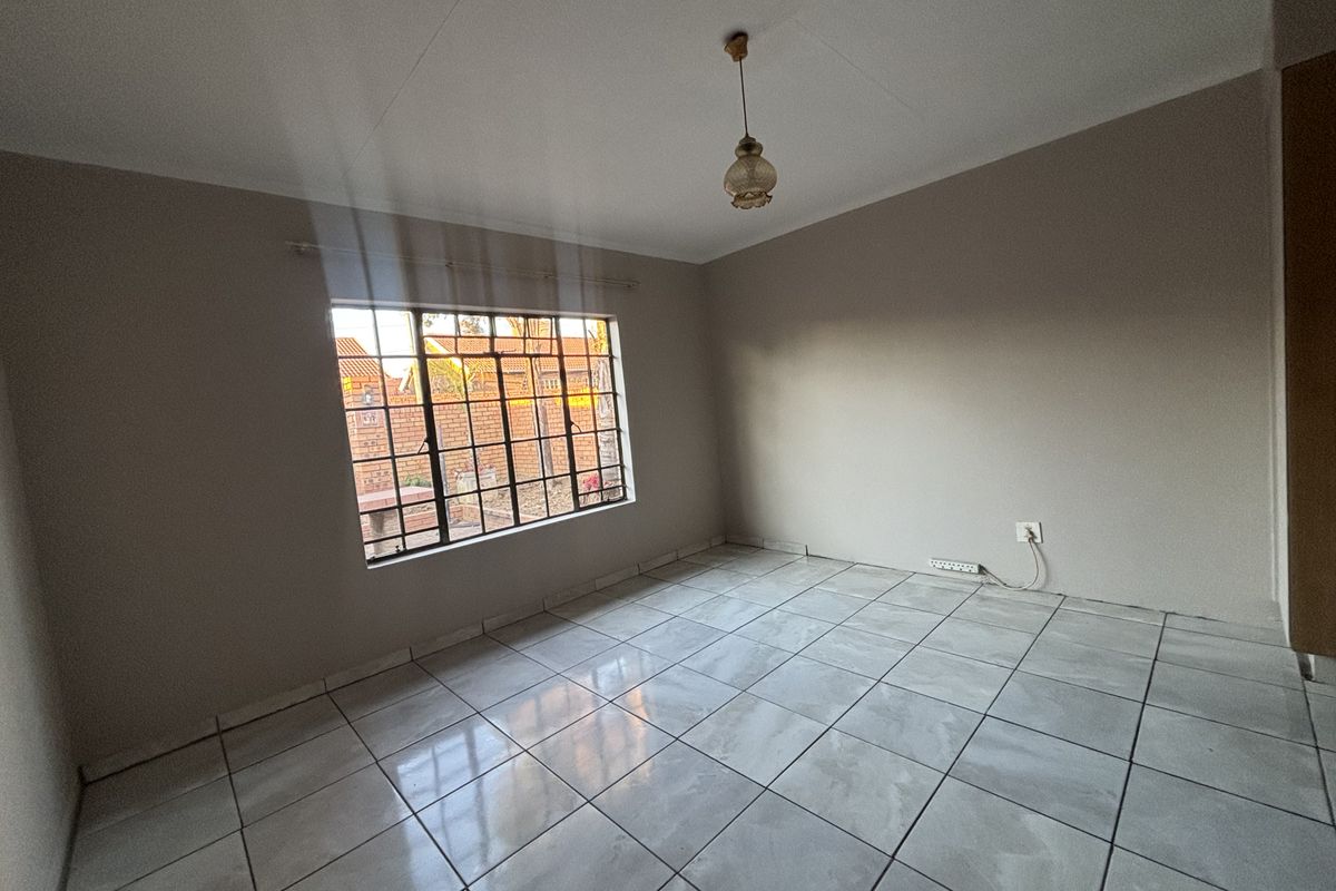 A clean, empty bedroom featuring neutral wall paint, tiled flooring, and a window fitted with security bars.