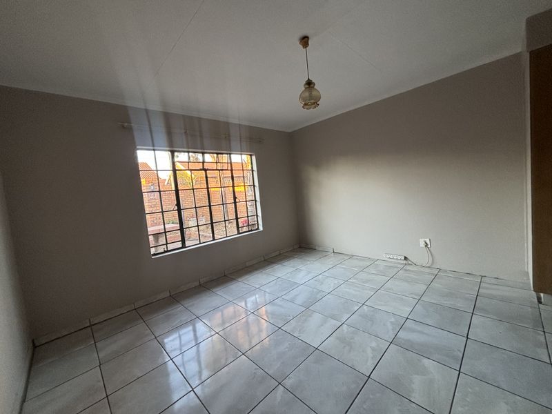 A clean, empty bedroom featuring neutral wall paint, tiled flooring, and a window fitted with security bars.