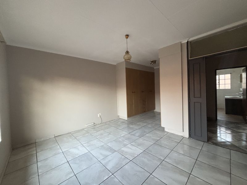 A spacious, empty bedroom featuring neutral wall tones, tiled flooring, and integrated built-in cupboards, offering a clean canvas for personalization.