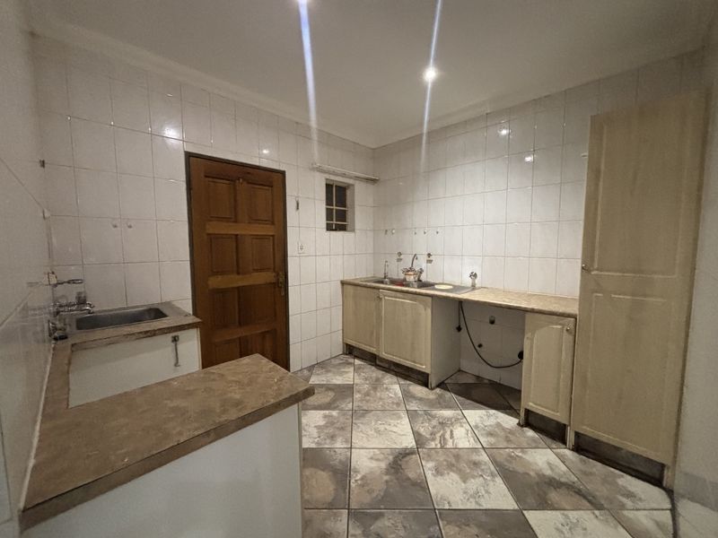 A functional scullery or utility area featuring tiled walls, laminate countertops, double sink, and built-in cabinetry with tiled flooring.