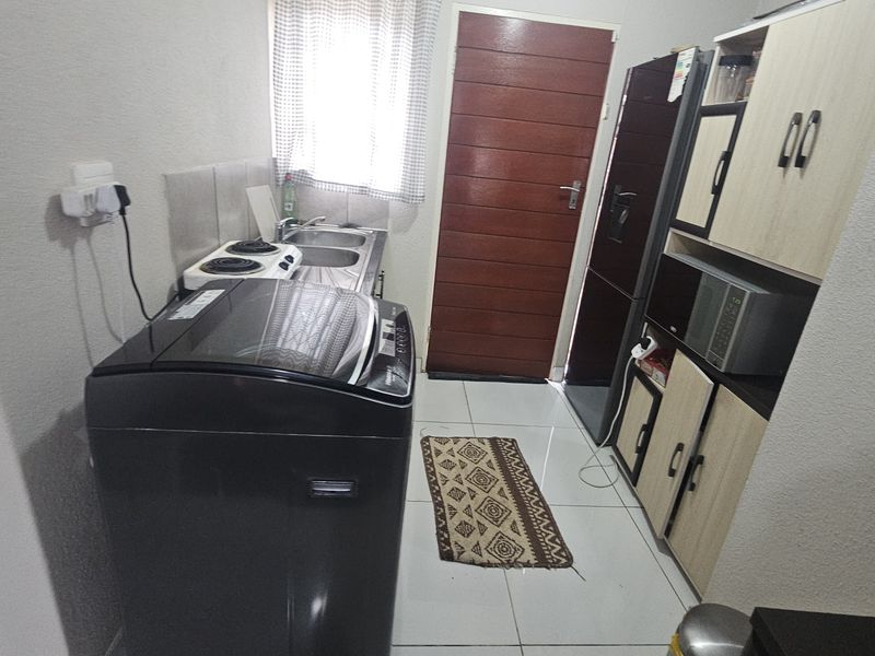 A functional laundry area featuring tiled flooring, built-in cabinetry, a stainless steel sink, and space for laundry appliances.