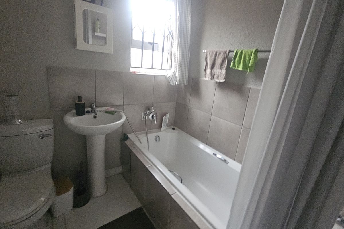 A functional bathroom featuring a pedestal basin, toilet, and bathtub with tiled splashbacks and a window with security bars.