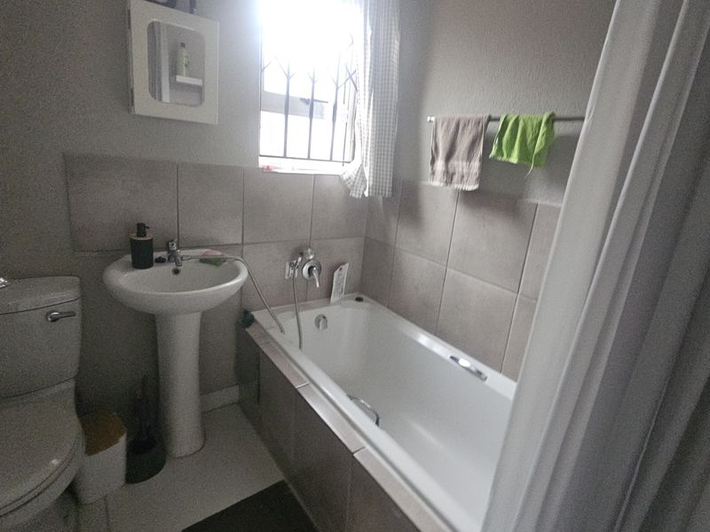 A functional bathroom featuring a pedestal basin, toilet, and bathtub with tiled splashbacks and a window with security bars.