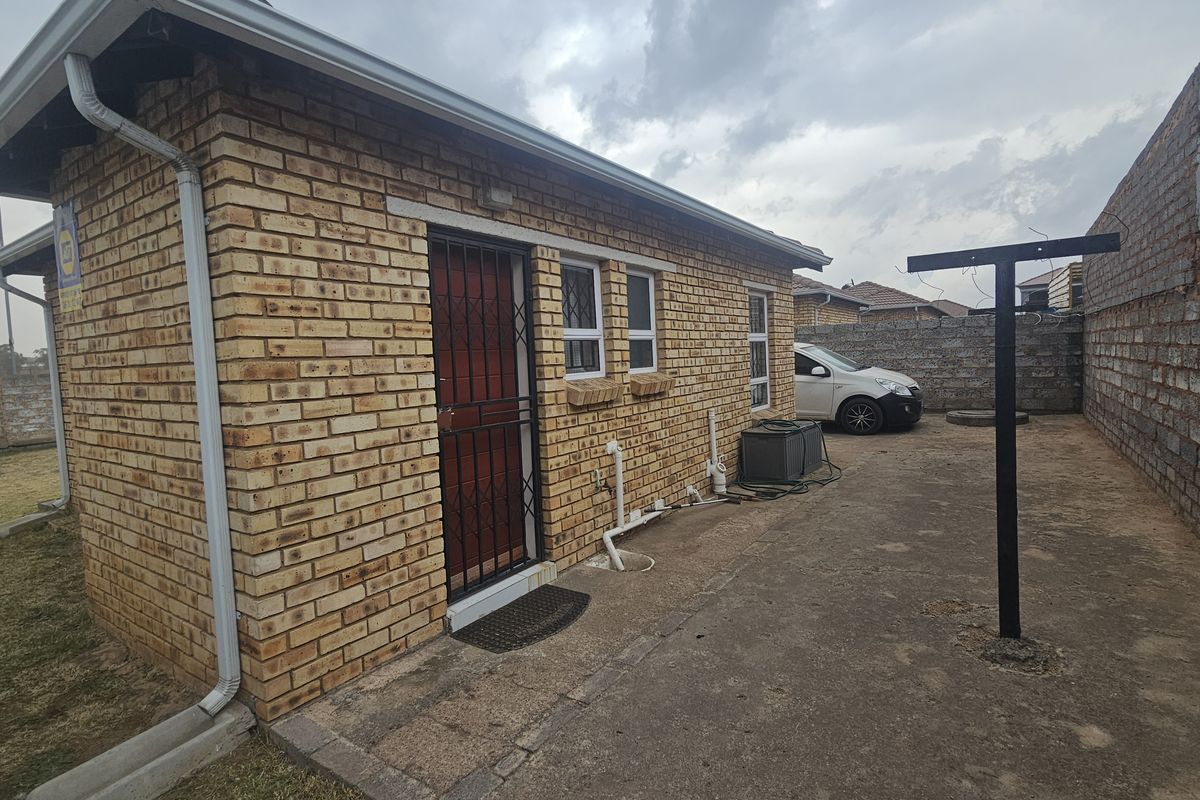 Rear exterior view of a face brick house featuring a security gate, concrete paving, and perimeter boundary walls.