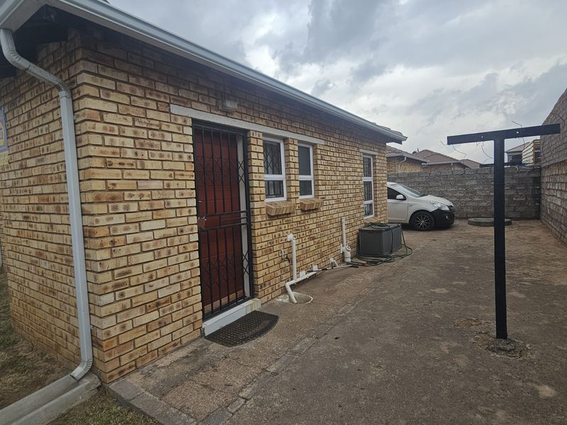 Rear exterior view of a face brick house featuring a security gate, concrete paving, and perimeter boundary walls.