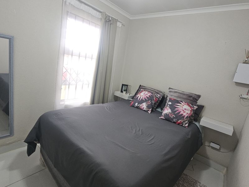 A compact bedroom featuring tiled flooring, a window with security bars, and wall-mounted floating bedside shelves.