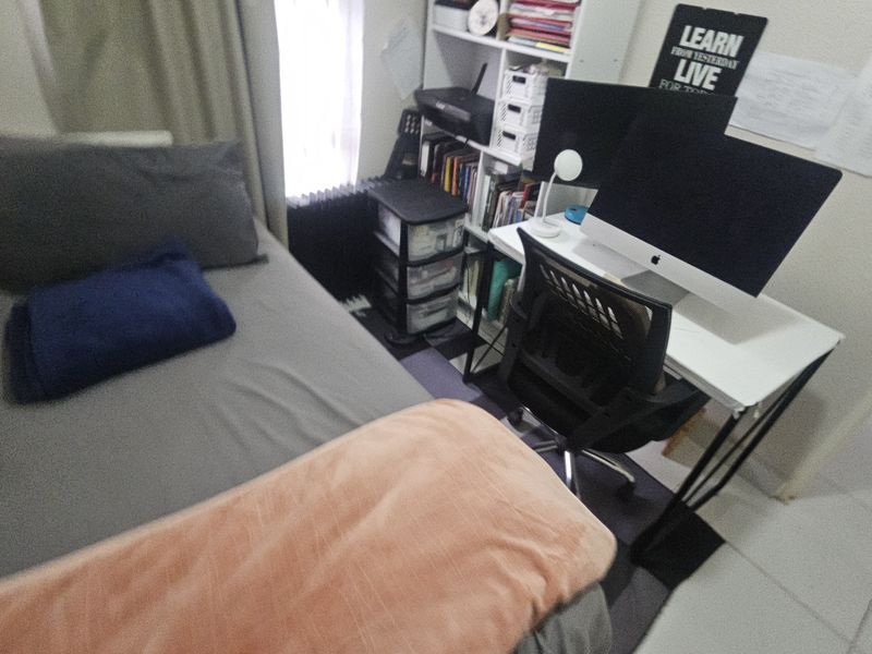 A compact bedroom featuring tiled flooring, currently utilized as a combined sleeping and workspace area.