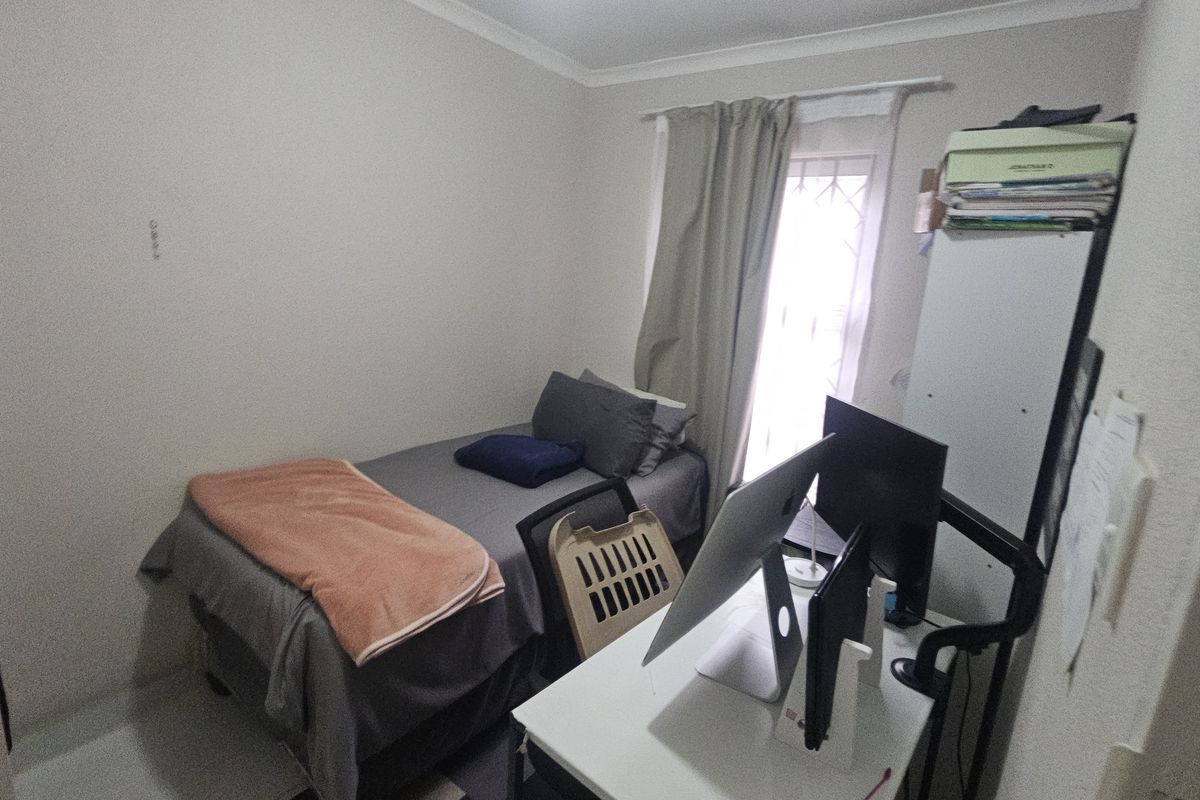 A compact bedroom featuring a window with a security gate and neutral wall finishes, suitable for use as a guest room or home office.