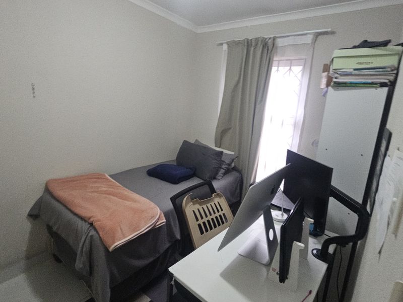 A compact bedroom featuring a window with a security gate and neutral wall finishes, suitable for use as a guest room or home office.