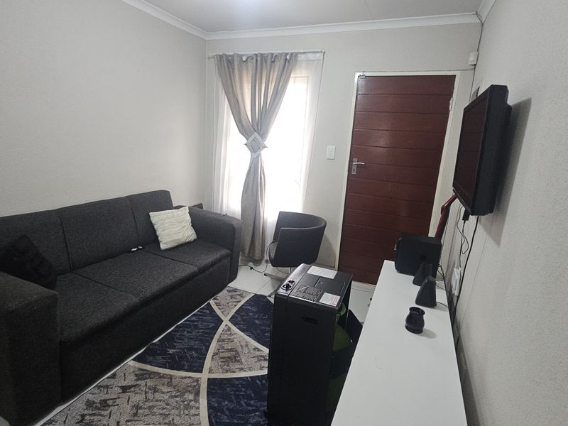 A compact living room featuring tiled flooring, neutral wall finishes, and a timber door, providing a functional and well-lit space.