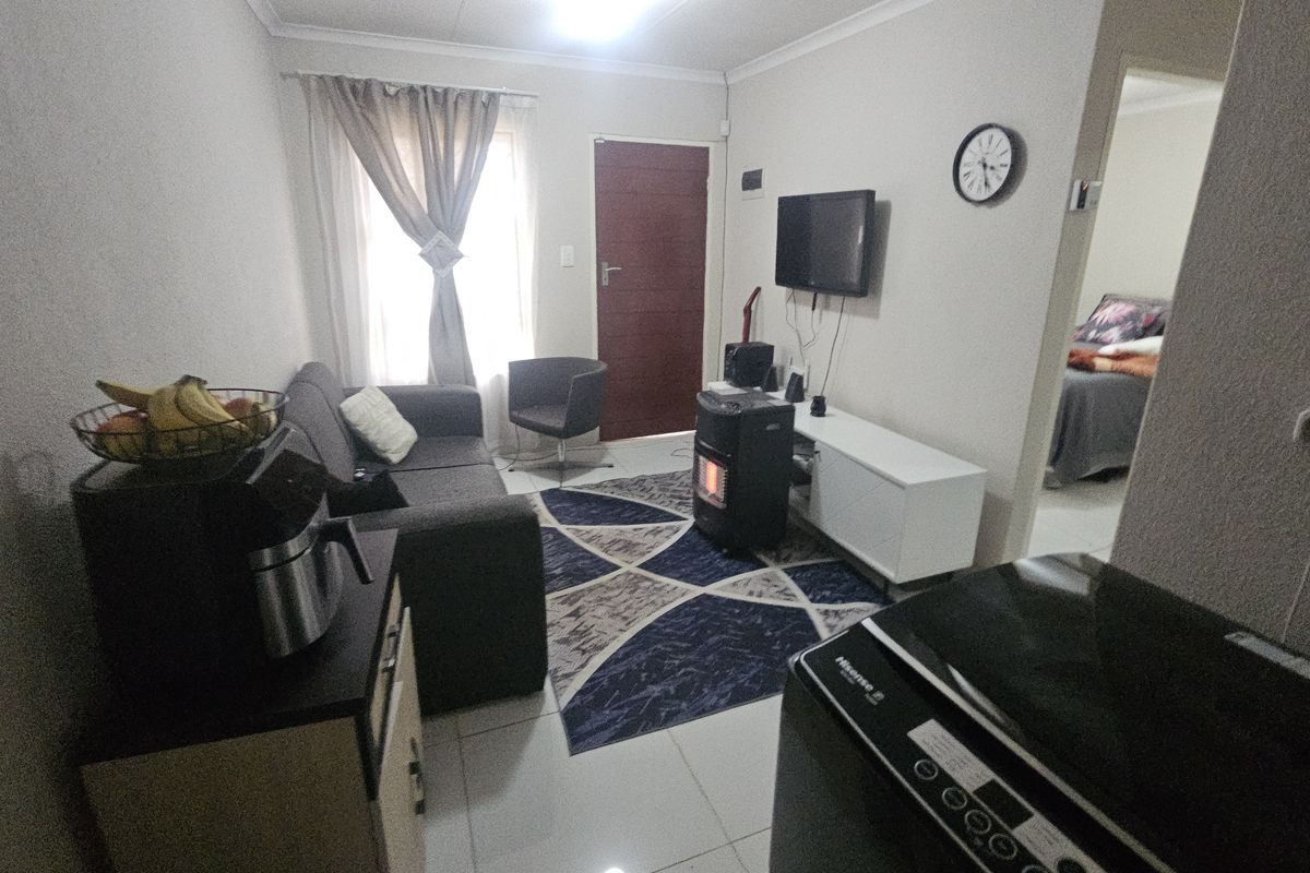 A compact living room featuring tiled flooring and neutral wall finishes, providing a functional space with direct access to adjacent rooms.