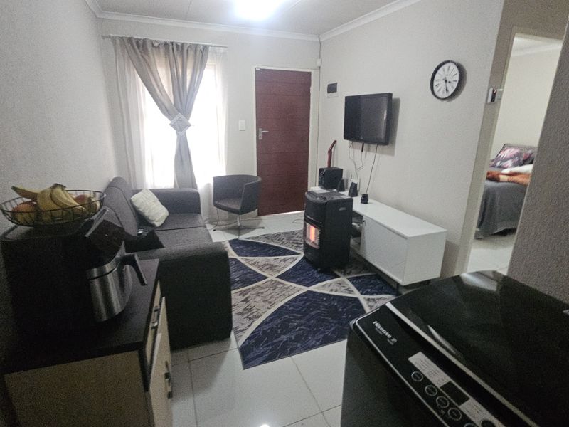 A compact living room featuring tiled flooring and neutral wall finishes, providing a functional space with direct access to adjacent rooms.