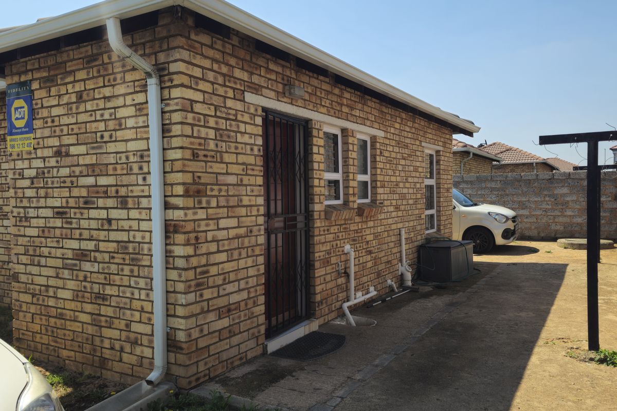 Rear exterior view of the face brick house featuring a security gate, aluminium windows, and concrete apron area.