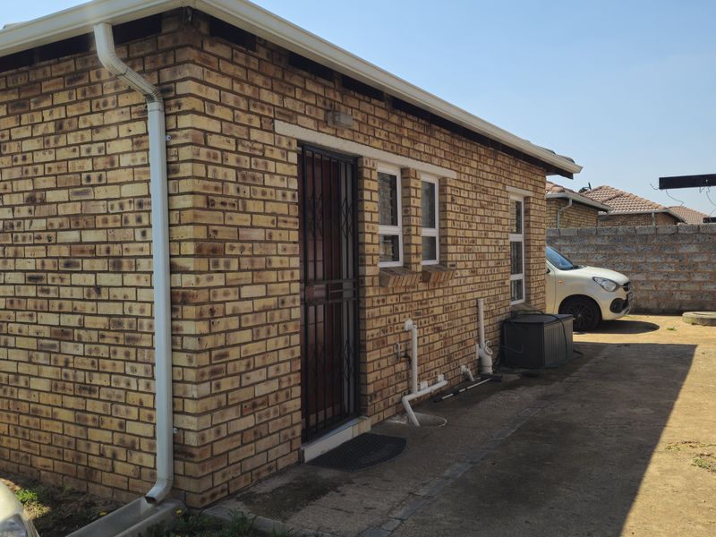 Rear exterior view of the face brick house featuring a security gate, aluminium windows, and concrete apron area.