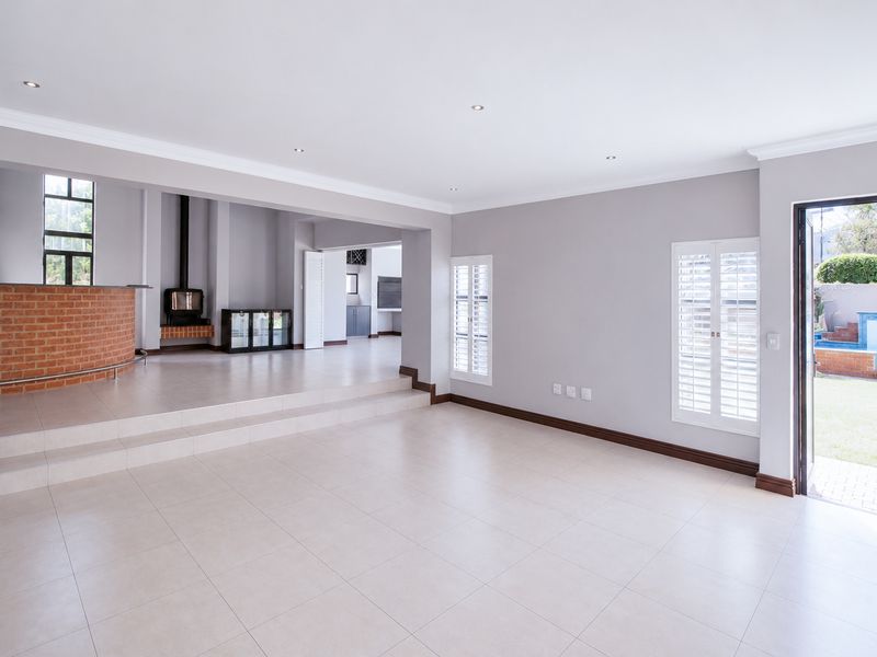 Spacious open-plan living area featuring a raised platform, brick fireplace with wood-burning stove, tiled flooring, and direct access to the garden.