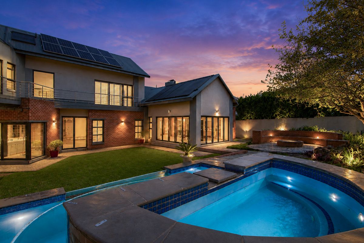 A beautifully landscaped rear exterior featuring a swimming pool, brick and render facade, solar panels, and a spacious patio area at twilight.