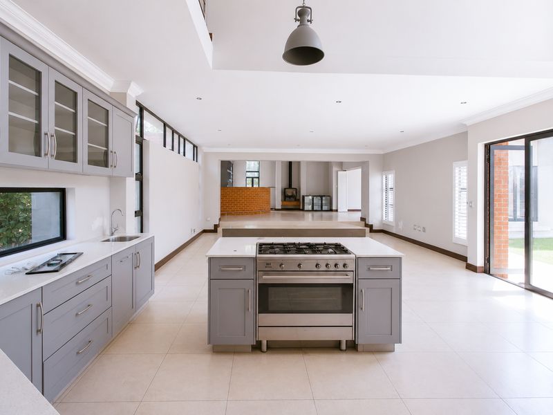 Spacious open-plan kitchen and living area featuring a central island with gas cooktop, modern cabinetry, tiled floors, and large sliding doors to the exterior.