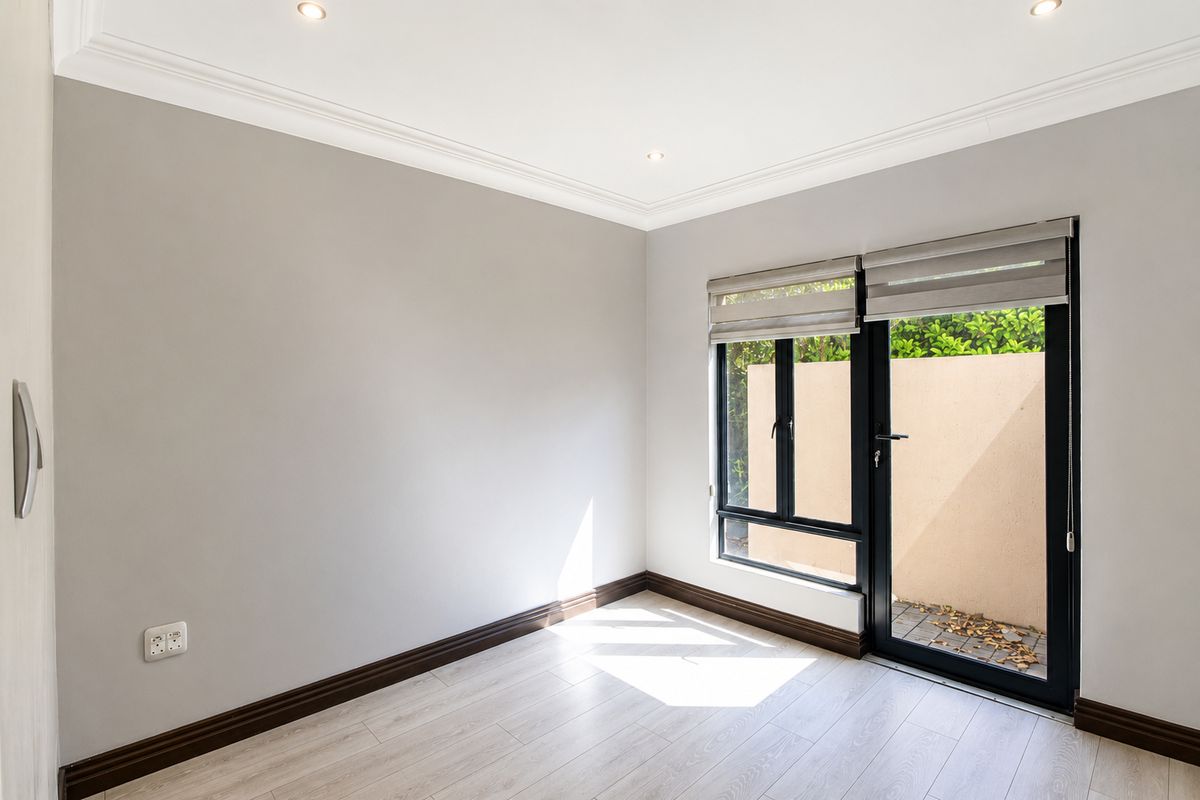 A bright, empty bedroom featuring modern laminate flooring, recessed downlighting, crown molding, and a glass door providing direct access to an outdoor area.