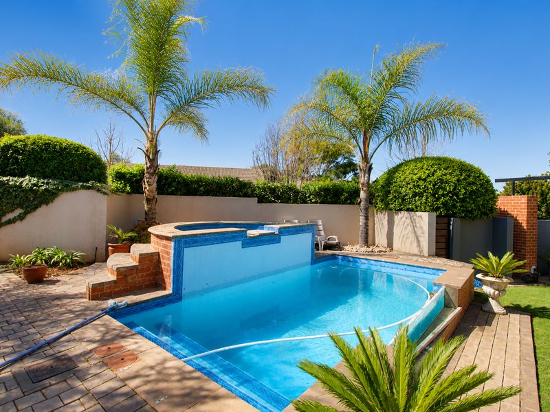 A well-maintained outdoor pool area featuring a raised spa, brick paving, and established landscaping, perfect for outdoor relaxation and entertainment.