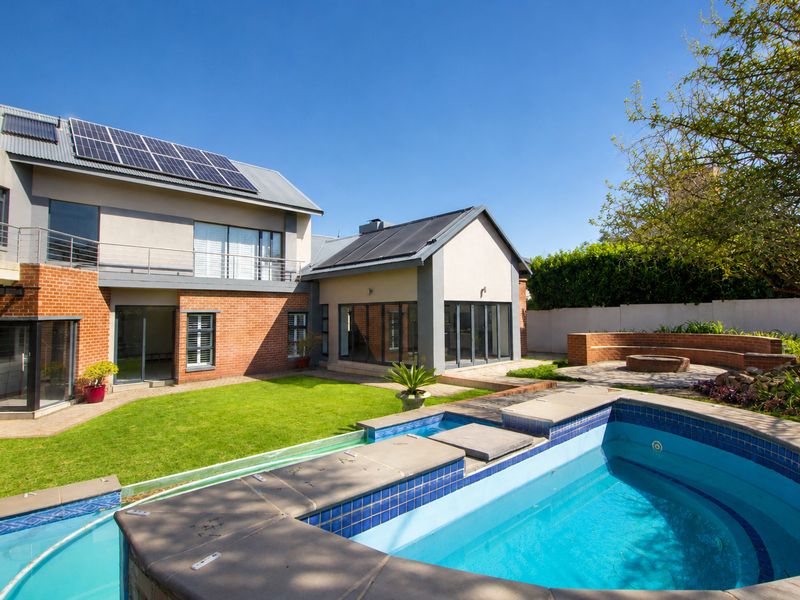 Spacious rear garden featuring a swimming pool, boma fire pit, and a modern two-story home with solar panels and balcony access.