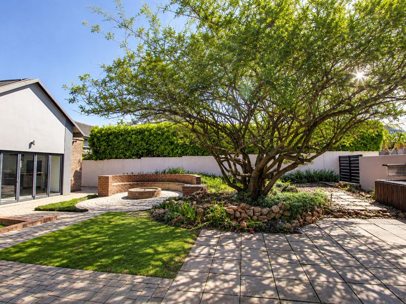 A well-maintained rear garden featuring a paved patio, a built-in brick fire pit with curved seating, and mature landscaping.