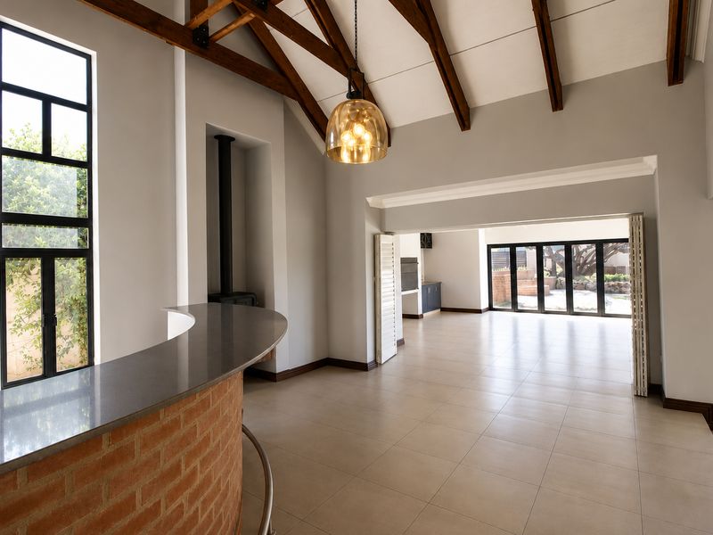 Spacious open-plan living area featuring exposed timber beams, a built-in brick bar, a fireplace, and large bi-fold doors leading to the outdoor space.