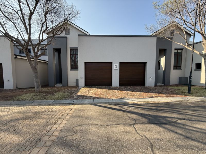 Front elevation of a modern townhouse featuring a double garage with dark wood-finish sectional doors and a paved driveway.