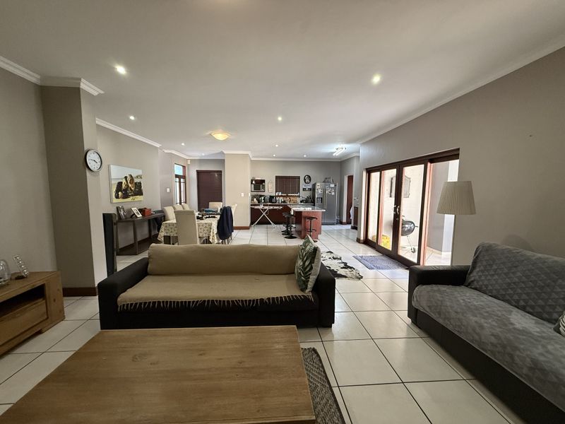 Spacious open-plan living and dining area featuring tiled floors, recessed lighting, and seamless flow to the outdoor patio through large sliding glass doors.
